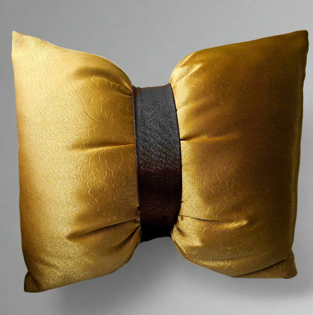 Two gold decorative pillows with a black ribbon on a light-colored couch.
