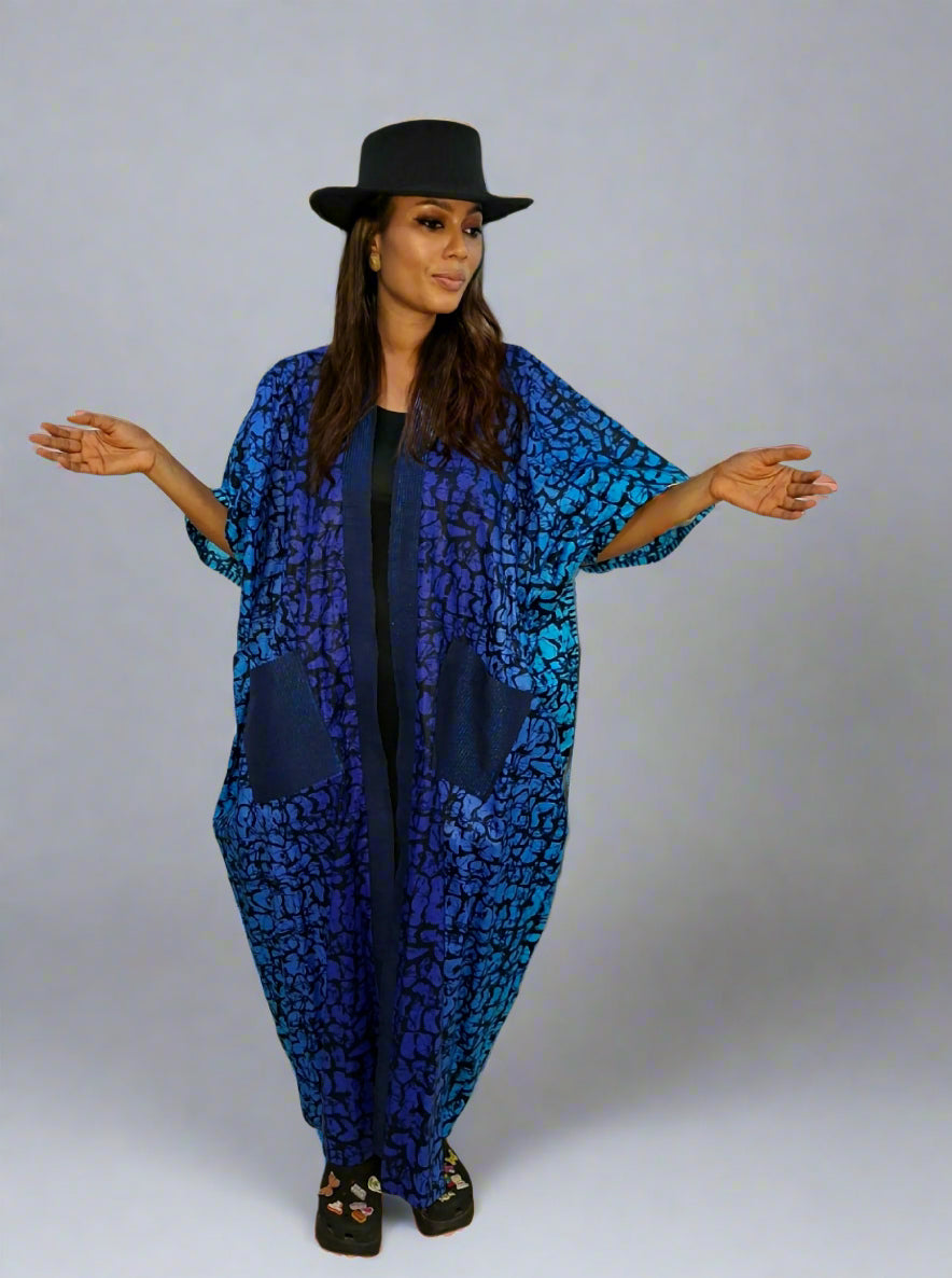 Woman wearing a blue patterned outfit with a black hat on a plain background