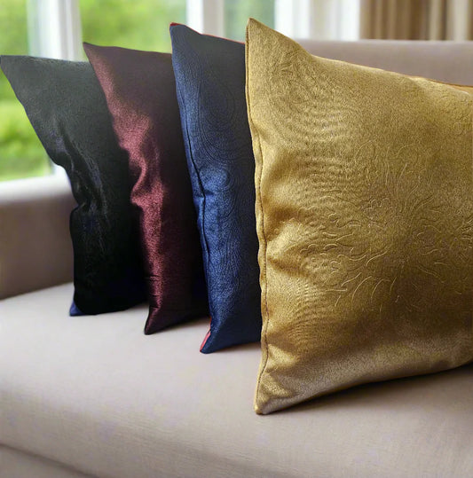 Four decorative pillows in black, burgundy, blue, and gold on a beige sofa.