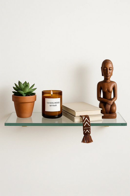 Glass shelf with a potted plant, candle, books, and wooden figurine on a white background