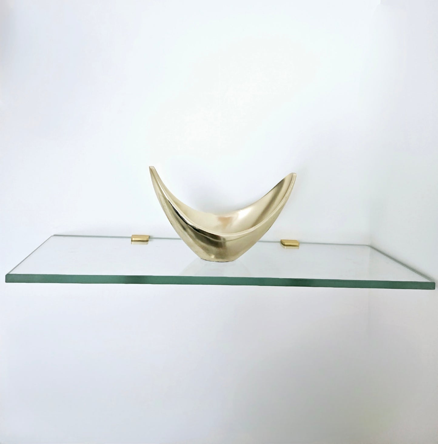 Glass shelf with a decorative brass bowl on a white background