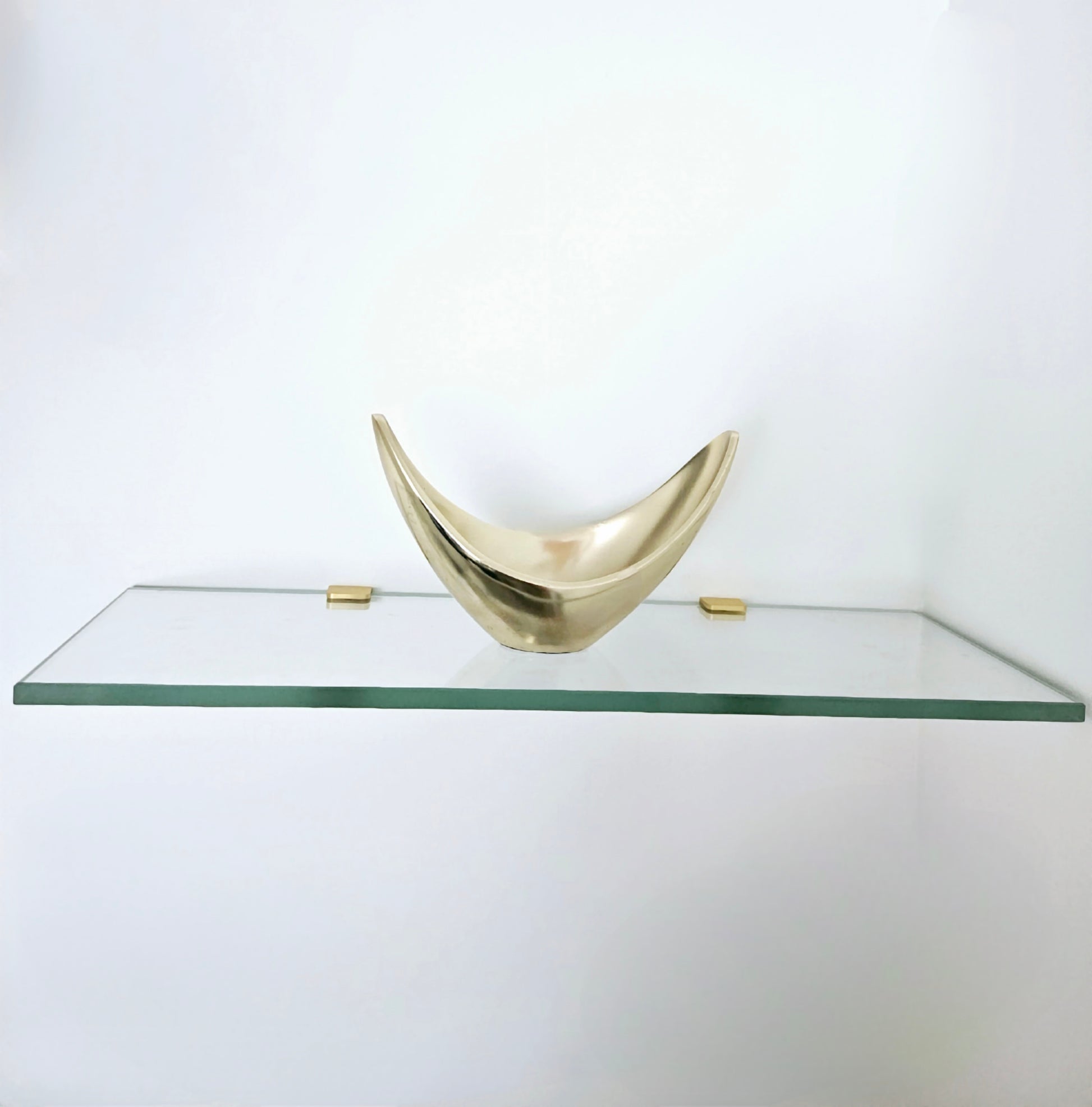 Glass shelf with a decorative brass bowl on a white background